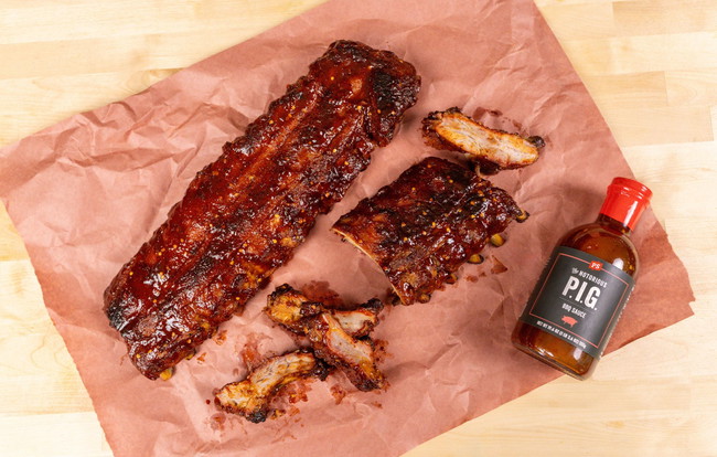 2 racks of ribs sitting on a piece of butcher paper with a bottle of PS Seasoning's Notorious P.I.G. rub along side it.
