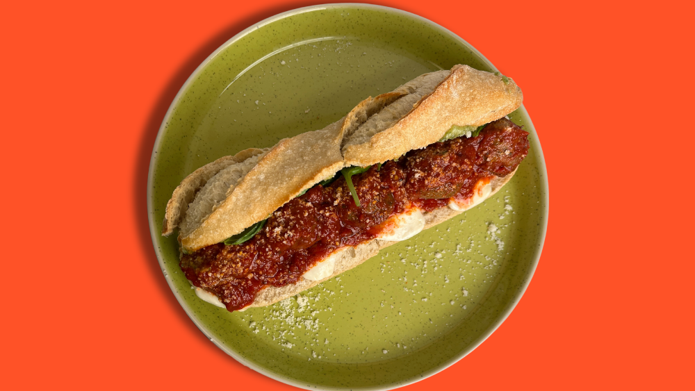 A baguette with saucy meatballs in the middle, all placed on a green plate
