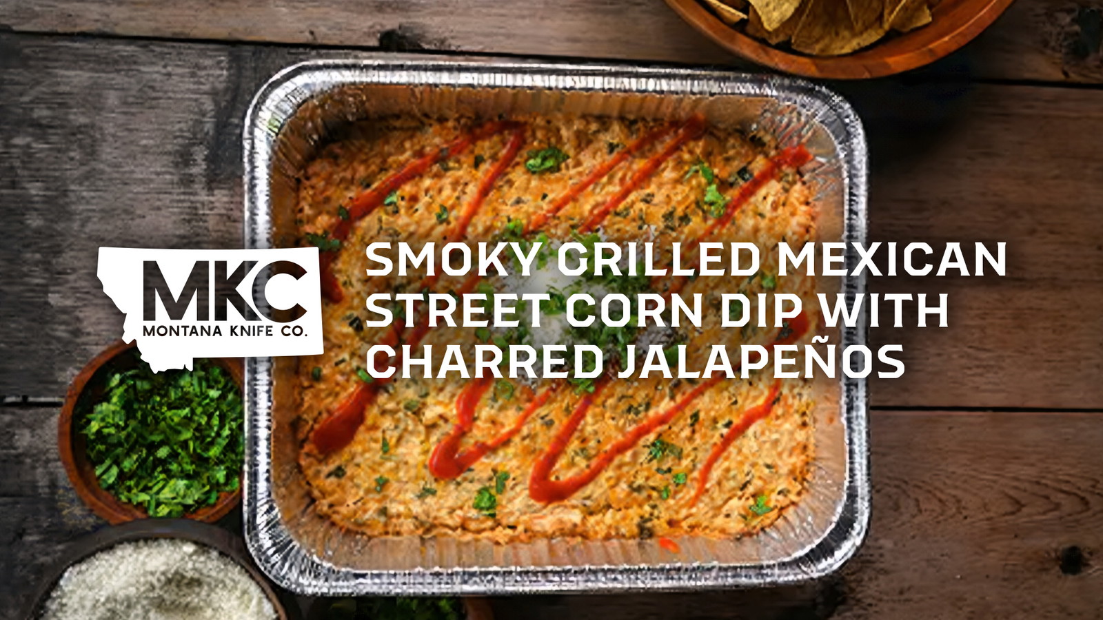 Creamy Mexican street corn dip in foil pan with hot sauce drizzles, surrounded by chips and fresh toppings.