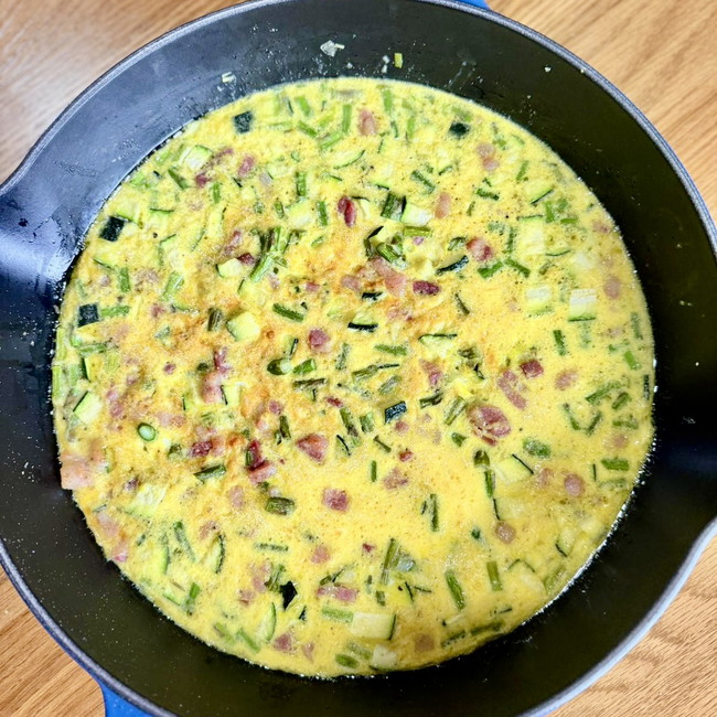 Overhead view of skillet with a frittata made of Parmigiano Reggiano, asparagus, pancetta, and zucchini