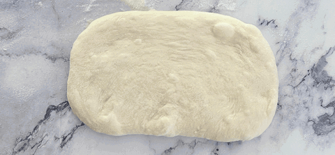 Image of Now we are ready to shape your baguettes. Sprinkle some flour onto your bench top and take the first circle. Flatten it out into a landscape rectangle shape.