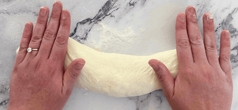Image of Place the dough seam side down and use your hands to roll the dough into a baguette shape, applying more pressure to the ends so they taper in a little.