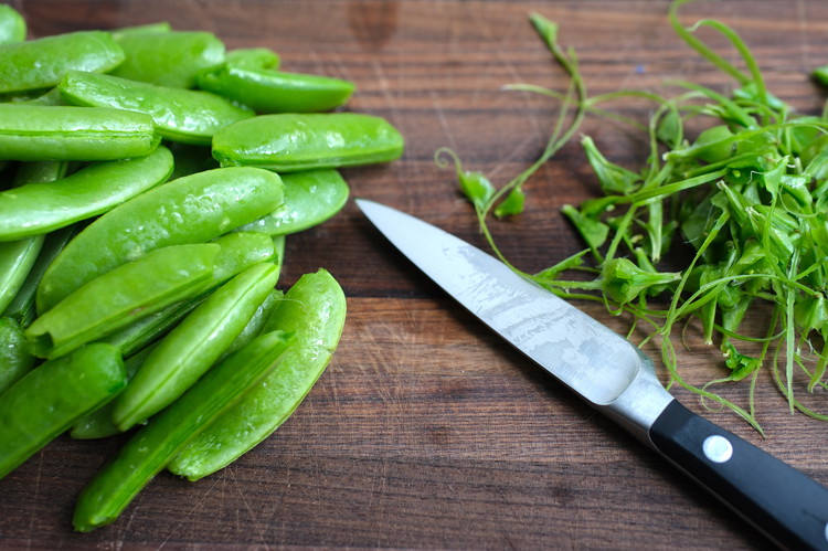Image of Prepare the snap peas by removing the fibrous ridge “string”.  You do this with a pairing knife by putting the tip of the sugar pea between your thumb and a knife (carefully).  You then cut/press and pull—this sound peel away...