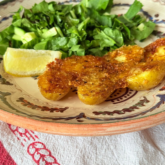 Plate of crispy potatoes accompanied by a salad and a lemon wedge