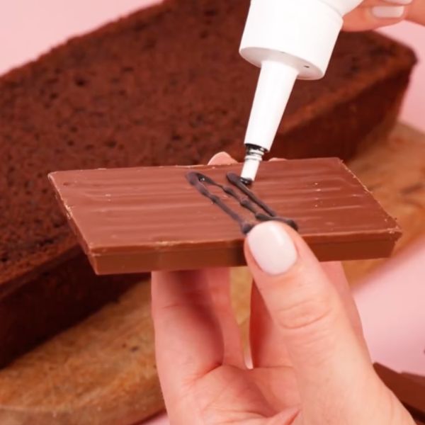 Image of Stelle nun die untere Hälfte mittig auf eine Platte. Platziere rundherum Riegel wie KitKat oder andere Schokoriegel, um die Truhenwände darzustellen.										