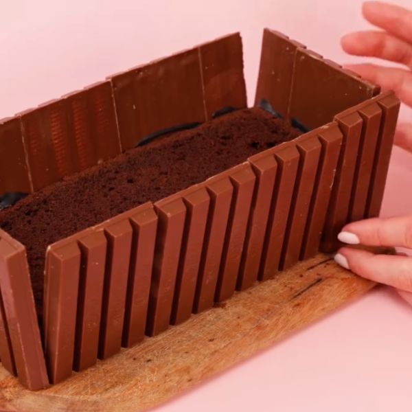 Image of Damit sie auch am Kuchen halten, verwende entweder etwas von der Kuchenglasur oder bspw. unseren Happy Drip in Midnight Black und Klebe die Schokoriegel so an den Seiten des Kuchens fest.