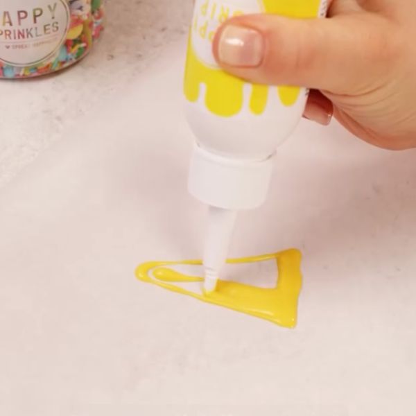 Image of Clownhut vorbereiten: Schmelze deinen Happy Drip wie auf der Flasche angegeben.Zeichne mit dem flüssigen Drip auf Backpapier einen kleinen, spitzen Clown-Hut und setze nach Lust und Laune Streifen oder Punkte darauf. Für das Bommel-Ende oben einfach eine kleine Kugel mit...