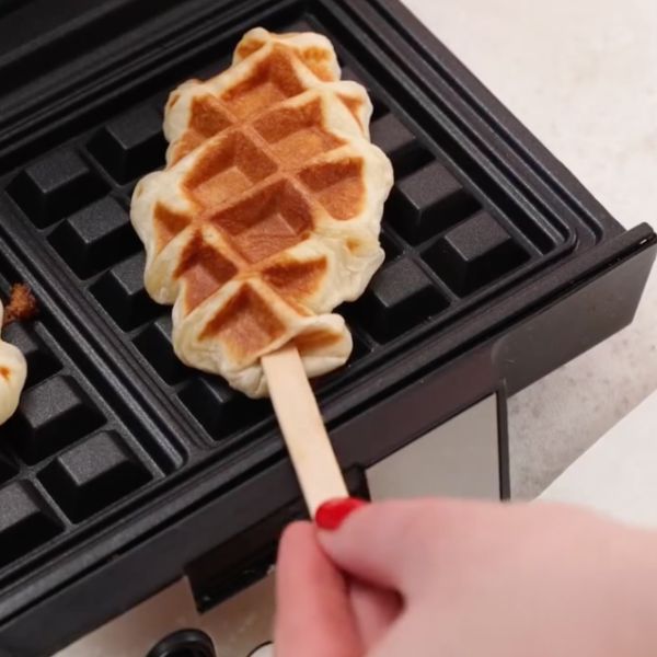 Image of Das Waffeleisen vorheizen, leicht fetten und die Croffel Pops nacheinander ausbacken – etwa 3–4 Minuten, bis sie goldbraun und herrlich knusprig sind. Einen Holzstiel mittig hinein drücken.