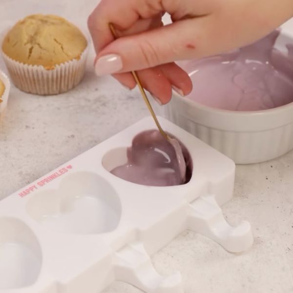 Image of Die Hälfte der weißen Schokolade schmelzen, in der Farbe nach Wahl einfärben und in die Cakesicle Form geben und bis zum Rand hochstreichen. Hier gerne jeweils eine dicke Schicht und das ganze 10 Minuten in den Kühlschrank oder Gefrierfach stellen.