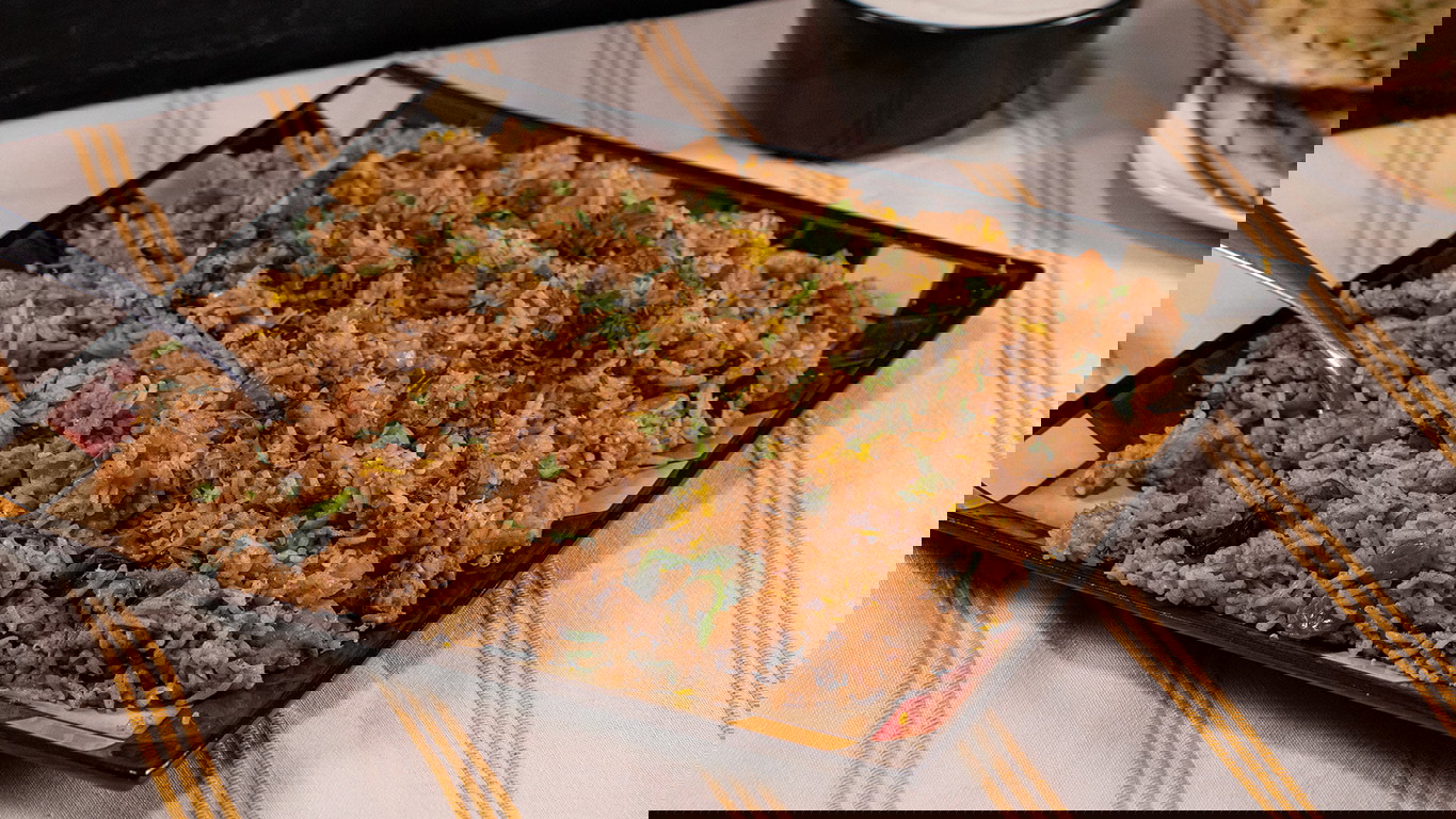 A large square plate of cooked basmati rice and diced Halal chicken mixed in aromatic seasoning, then topped with fresh mint and lemon zest.