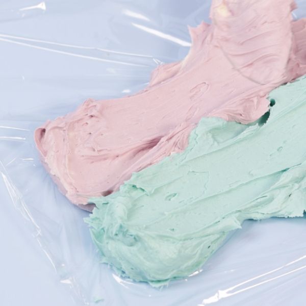 Image of Schuppen gestalten:2 Farben der eingefärbten Buttercreme nebeneinander auf Frischhaltefolie streichen, vorsichtig zusammenrollen und dann in einen Spritzbeutel mit einer Lochtülle geben.
