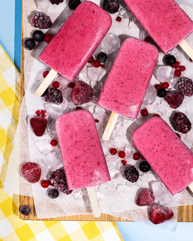 A tray of fresh summer berry smoothie ice lollies over ice