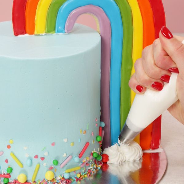 Image of Mit einem Spritzbeutel (Sterntülle) setzt du fluffige Wolkentuffs: Auf die Torte, direkt vor den Keksbogen und auf die Tortenplatte, dort wo der Regenbogen „landet“.