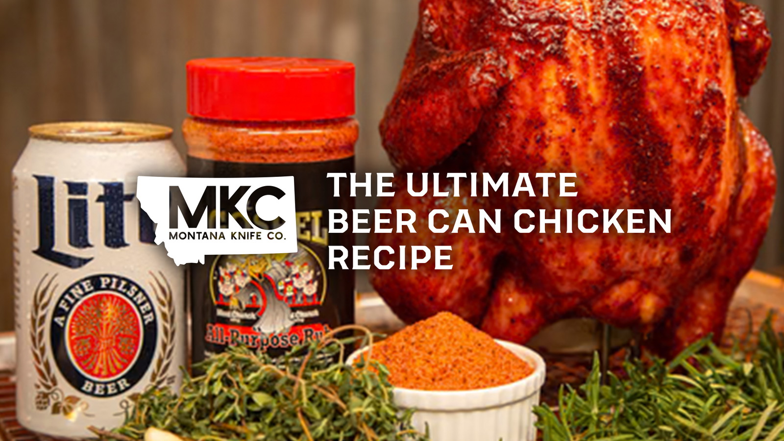 Seasoned whole chicken, positioned upright beside a bottle of seasoning, a beer can, and sprigs of fresh herbs.