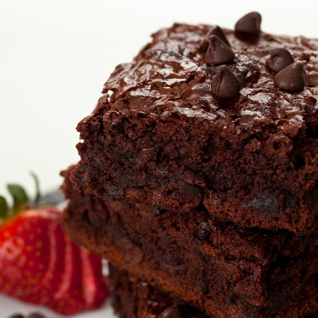 Close-up of rich, fudgy brownies made with Wild West Waffles Coffee Maple Syrup, stacked on a plate and topped with chocolate chips, served alongside fresh strawberries.