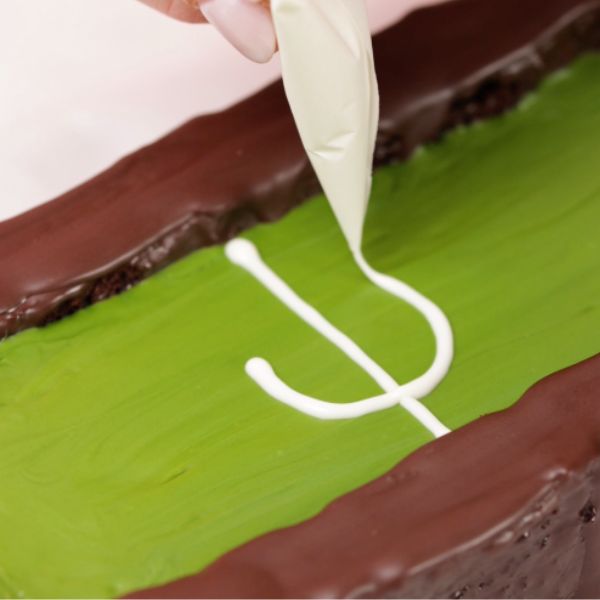 Image of Schmelze den Creamy White Drip, fülle ihn in einen kleinen Spritzbeutel und zeichne Spielfeldlinien ein. Trocknen lassen.