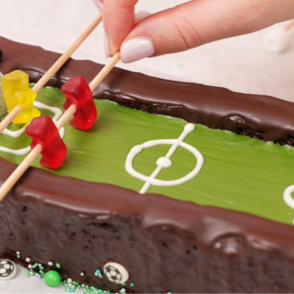 Image of Gummibärchen auf Holzstäbe spießen (abwechselnd je Teamfarbe) und auf dem Kuchen platzieren. Eine Schokokugel in die Mitte setzen – Anpfiff! ⚽️