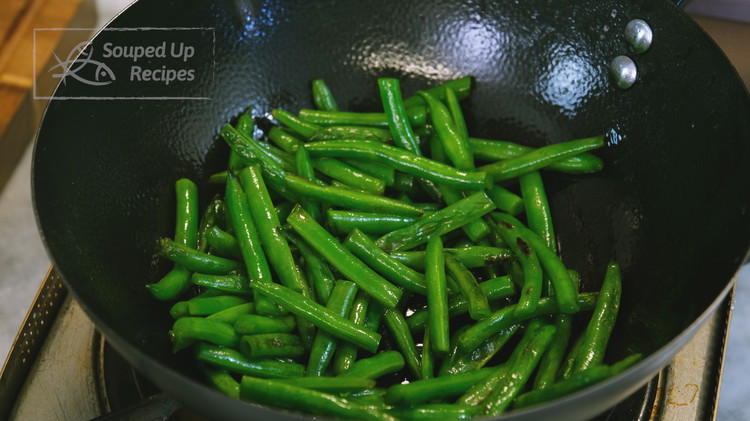 Image of Add 1.5 tbsp of oil, green beans, and 1/4 tsp of salt to the wok and stir over low heat for 8-10 minutes or until the green beans are slightly roasted.