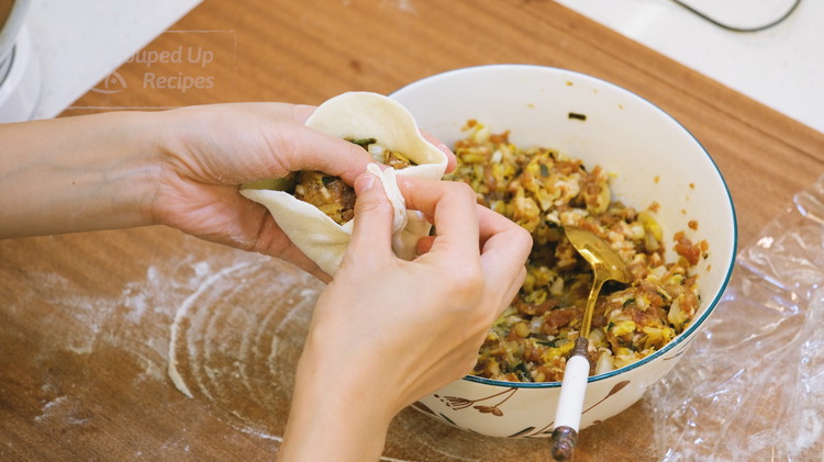 Image of Put some filling in the middle. If you are a beginner, don't put too much. Pinch the edge to create the first pleat. Use your other hand to help stretch, fold, and pinch the wrapper; Repeat that all the way around...