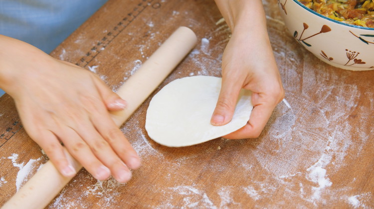 Image of Take one piece of dough. Flatten it with your hand. Use a rolling pin to roll it bigger. Then pick it up. Roll the edge back and forth. The left hand rotates the dough. Repeat that and you will get...