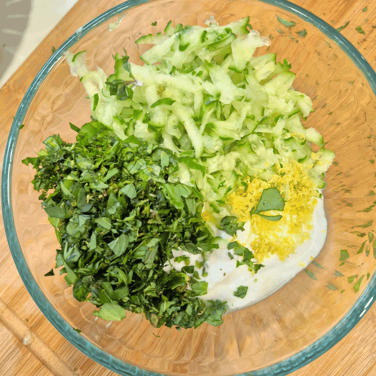 Image of In a medium bowl, combine the cucumber, yogurt, lemon juice, zest, olive oil, garlic, salt, pepper and herbs. 