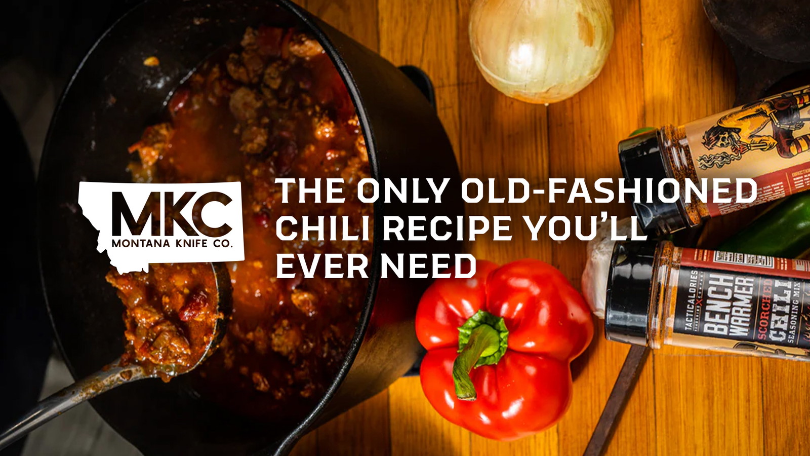 Cast-iron pot of old-fashioned chili with spoon, bell pepper, and onion.