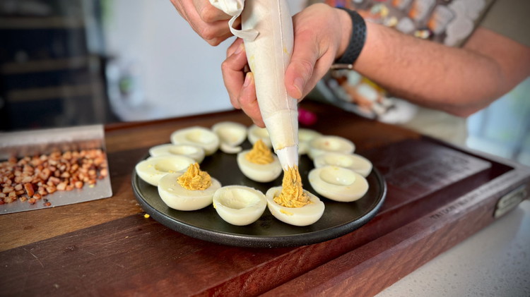 Image of using either a piping bag or a zip lock bag with the corner cut off, pipe egg mixture into egg white halves. 