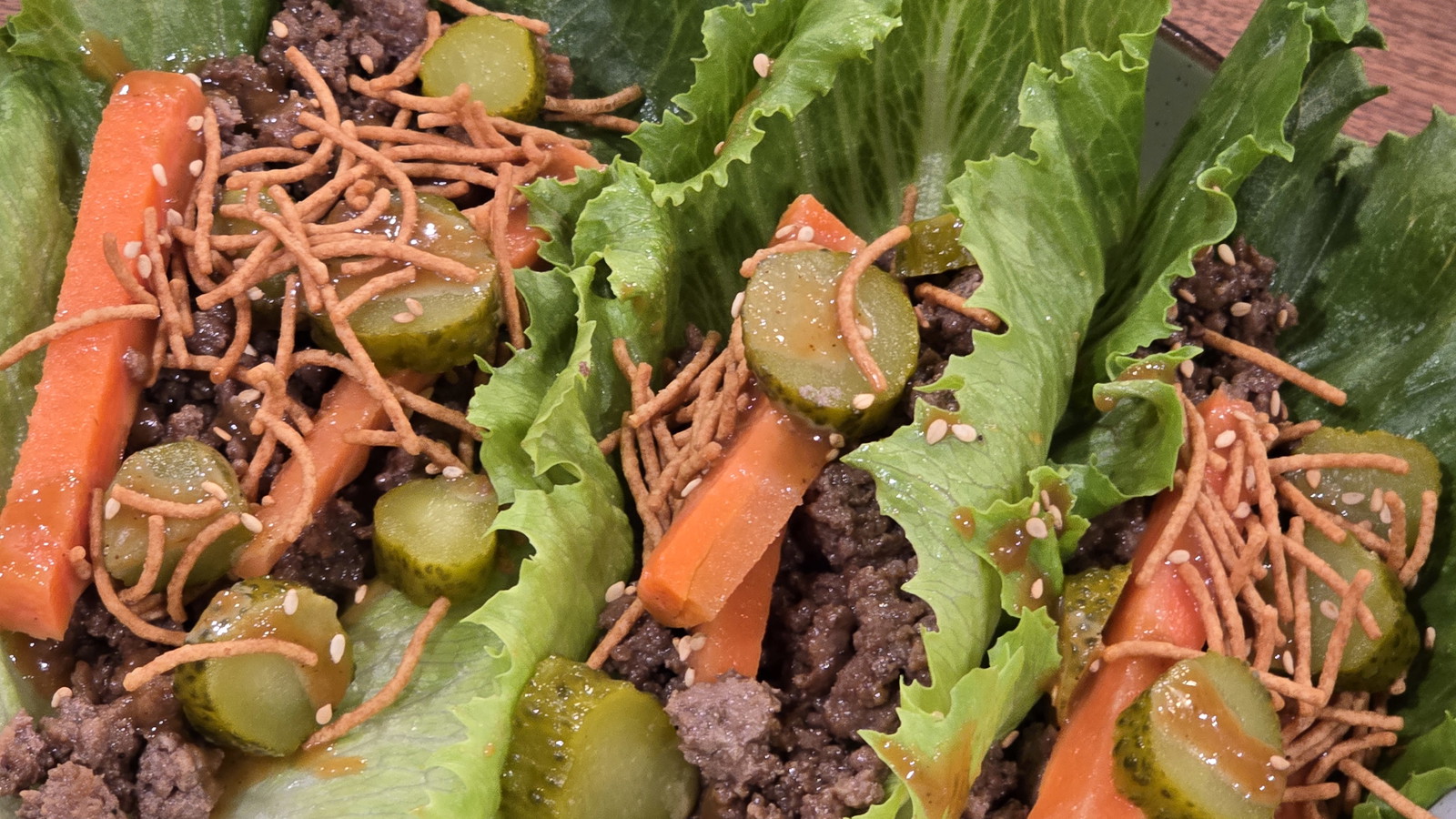 “Ground beef lettuce wraps with pickled carrots, chopped pickles, crunchy noodles, and sesame seeds served in fresh lettuce boats.”