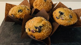 Four large bakery-style blueberry muffins with golden, domed tops and bursts of baked blueberries, arranged neatly on a serving platter.
