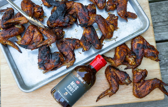 Smoked chicken wings on a tray and cutting board, caramelized with PS Seasoning Mug Shot Root Beer BBQ Sauce. Full, meaty wings seasoned with Cock-A-Doodle Brew BBQ rub, smoked to perfection with a crispy exterior and sticky-sweet glaze. smoked chicken wings recipe, root beer BBQ wings, PS Seasoning Mug Shot sauce, beer can chicken rub wings, Pro Max smoker recipes, sweet and smoky BBQ wings, easy smoked chicken wings