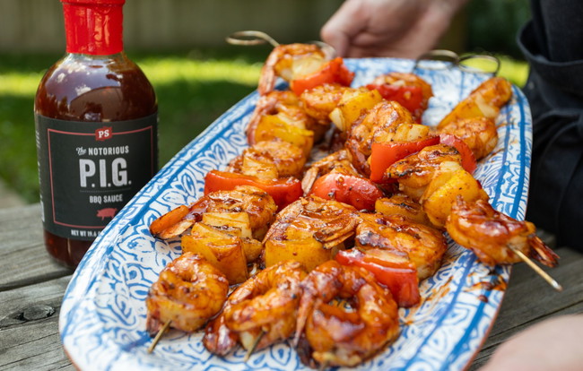Grilled shrimp skewers with red bell pepper and onion, basted in PS Seasoning Notorious PIG BBQ Sauce and seasoned with On The Rocks Steak Seasoning, served on a patterned blue and white platter. BBQ shrimp skewers recipe, grilled shrimp with vegetables, Notorious PIG BBQ Sauce shrimp, On The Rocks Steak Seasoning, summer shrimp recipes, smoky BBQ shrimp kabobs, easy grilled shrimp skewers