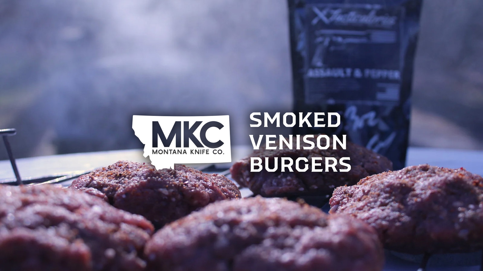 Close-up of smoked venison burgers cooking on a grill with smoke rising.