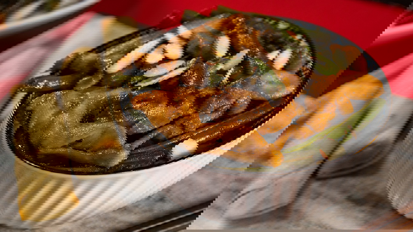 A white bowl of chicken stir fry of fresh string beans and juicy Halal chicken thighs coated in a savory sauce and topped with sliced almonds. Served with Halal chicken spring rolls.