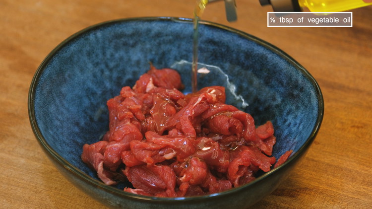 Image of Last, add a drizzle of vegetable oil and mix to coat the beef. This will prevent the meat slices from sticking together while cooking. Set the beef aside for 10 minutes.