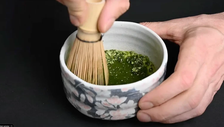 Image of Using the bamboo whisk, first stir gently to combine powder and water. Then whisk briskly in a zigzag (M or W) motion with your wrist until a fine foam forms on the surface (about 20–30 seconds).