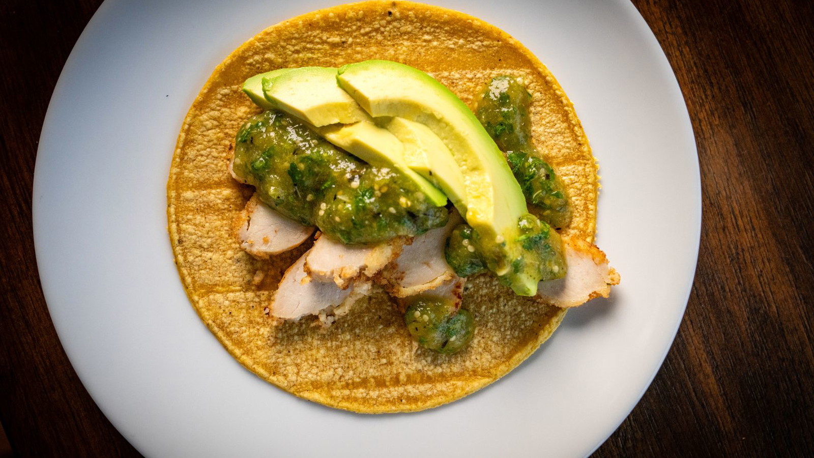 Chicken taco topped with green salsa and avocado