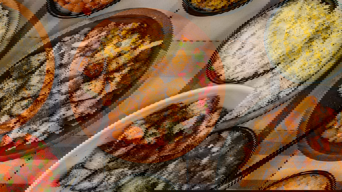 Top down image of a burrito bowl of cilantro lime rice, pico de gallo, grilled corn, pinto beans, Monterey Jack cheese, and juicy bites of Halal chicken. Served surrounded by each individual ingredient.