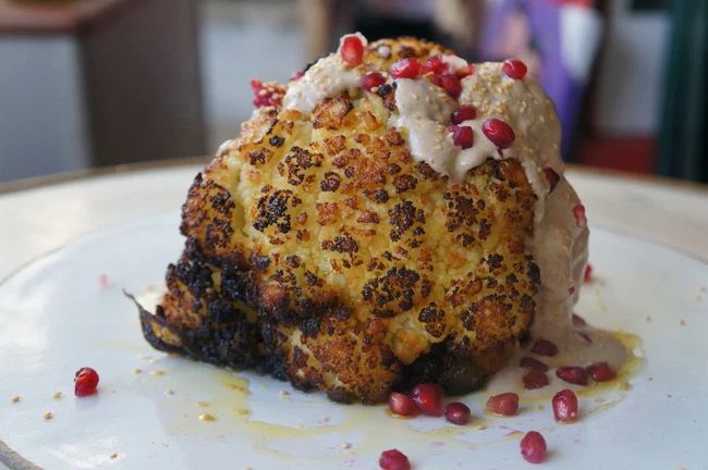 Image of Whole Head Of Roasted Cauliflower with tahini, toasted sesame seeds, pomegranate and fresh parsley