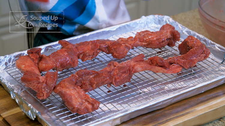 Image of Wrap a baking pan with tinfoil. Put a baking rack in the baking pan and place the marinated pork strips on the rack with some space between each other. Reserve the extra marinade left in the bowl.