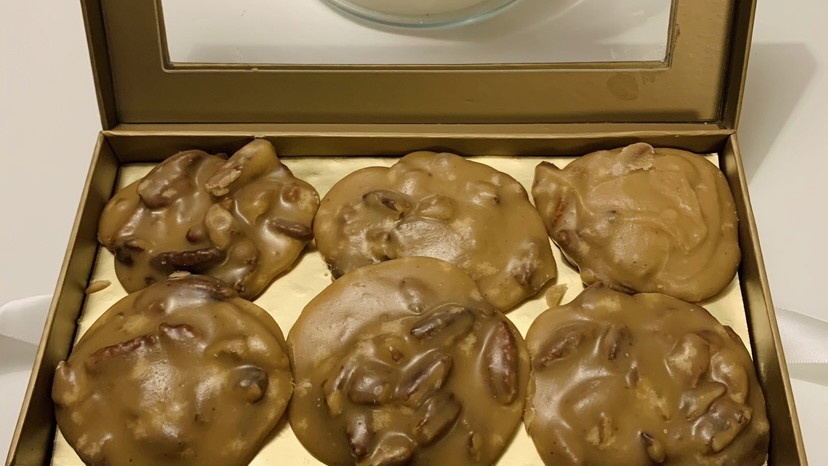 Round, rustic pecan pralines with a glossy, caramel-brown surface, studded with whole pecan halves and set on parchment paper.