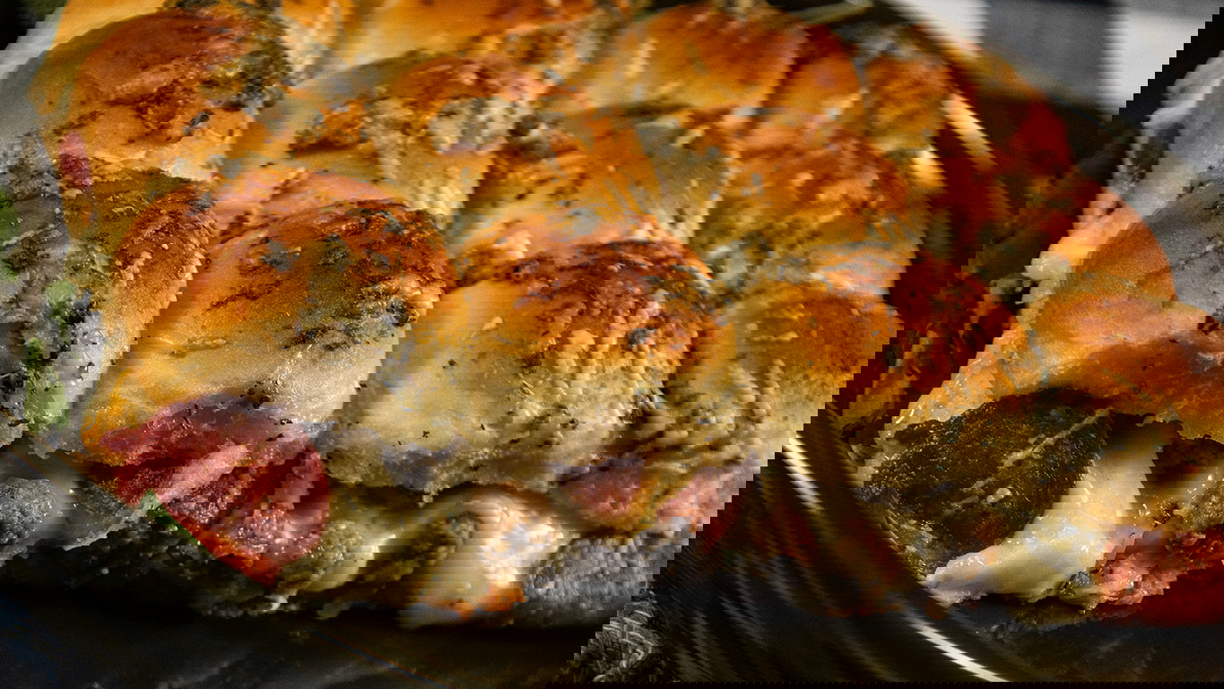 A tray of sliders filled with homemade pizza sauce, melty cheese, and meaty beef topping and beef pepperoni, coated in garlic butter and baked to a perfect golden brown.