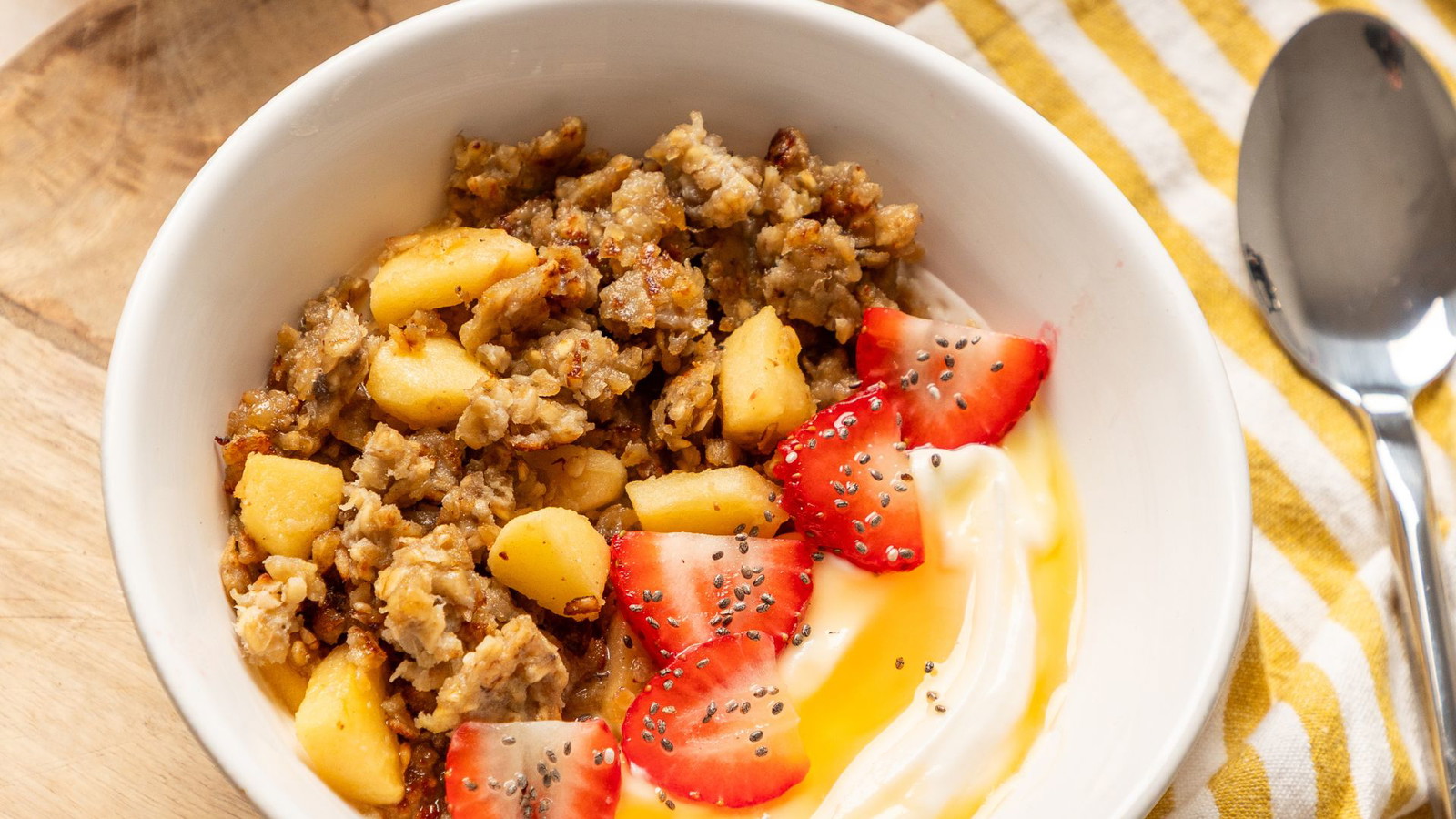Image of a bowl filled with scrambled oats, apple, strawberries, Greek yoghurt and Hilltop Blossom Honey