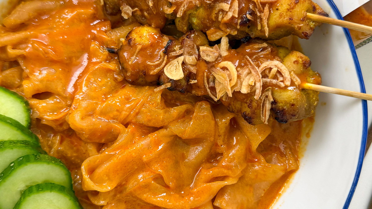 Thai peanut sauce rice paper noodles topped with chicken satay skewers, fresh herbs, and crushed peanuts in a bowl – quick Thai-inspired dinner.