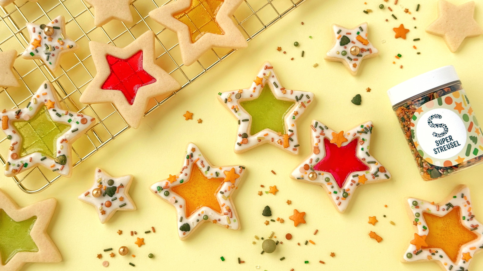 Sterkoekjes met glinsterende snoepvulling, witte drip en kleurrijke sprinkles op een bakmat