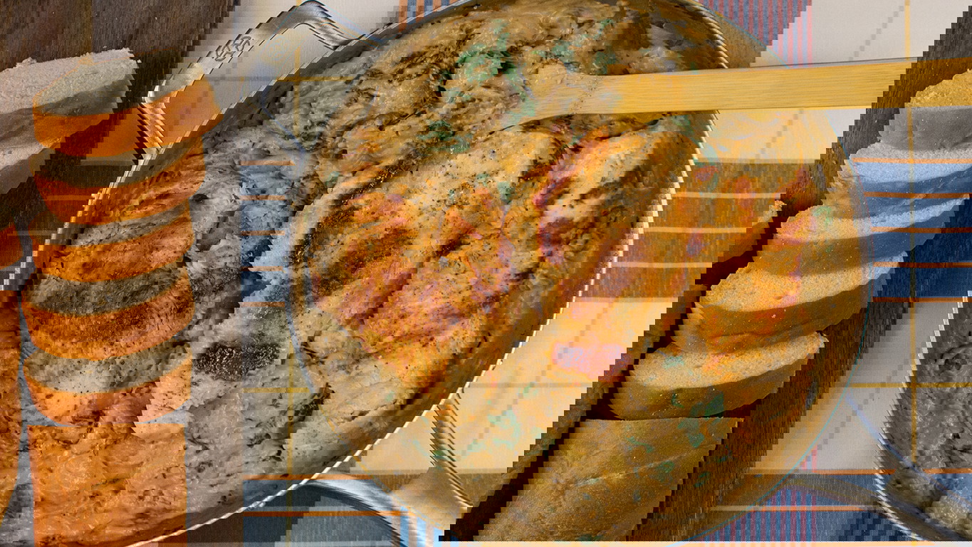 Top down image of a pan of golden-brown Halal chicken breast in a creamy sauce with tender gnocchi, spinach, and mushrooms served alongside a sliced loaf of bread.