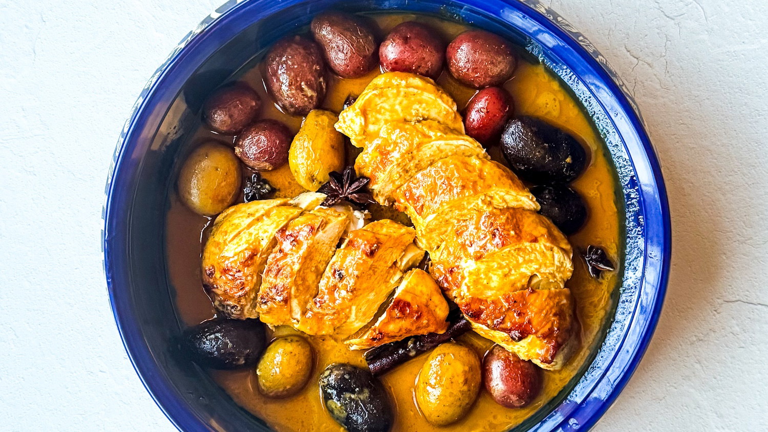 Baked chicken and potatoes topped with creamy Thai coconut curry sauce, served in a rustic baking dish and garnished with fresh herbs.