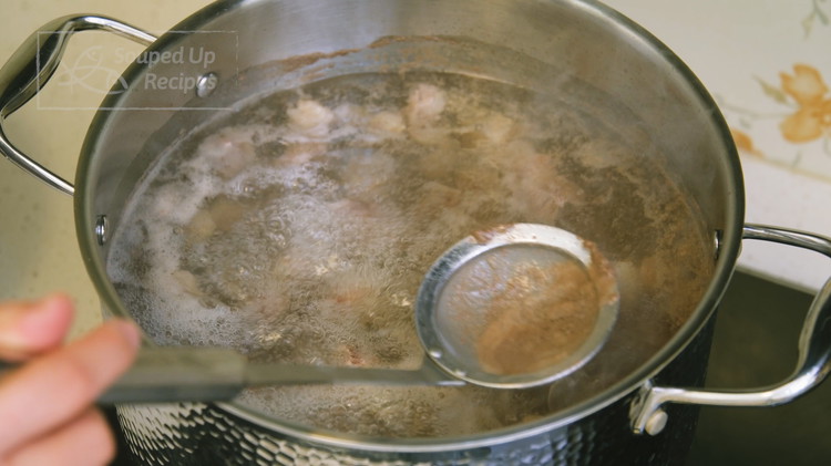 Image of Add the beef to a big stock pot, pour in  2.5 liters of water, and bring it to a boil over medium heat. Use a sieve to skim the foamy scum, then take the beef out and set it aside to drain.