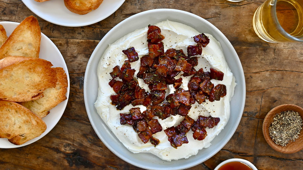 Whipped Goat Cheese with Candied Bacon on a plate on a table with bread on a table