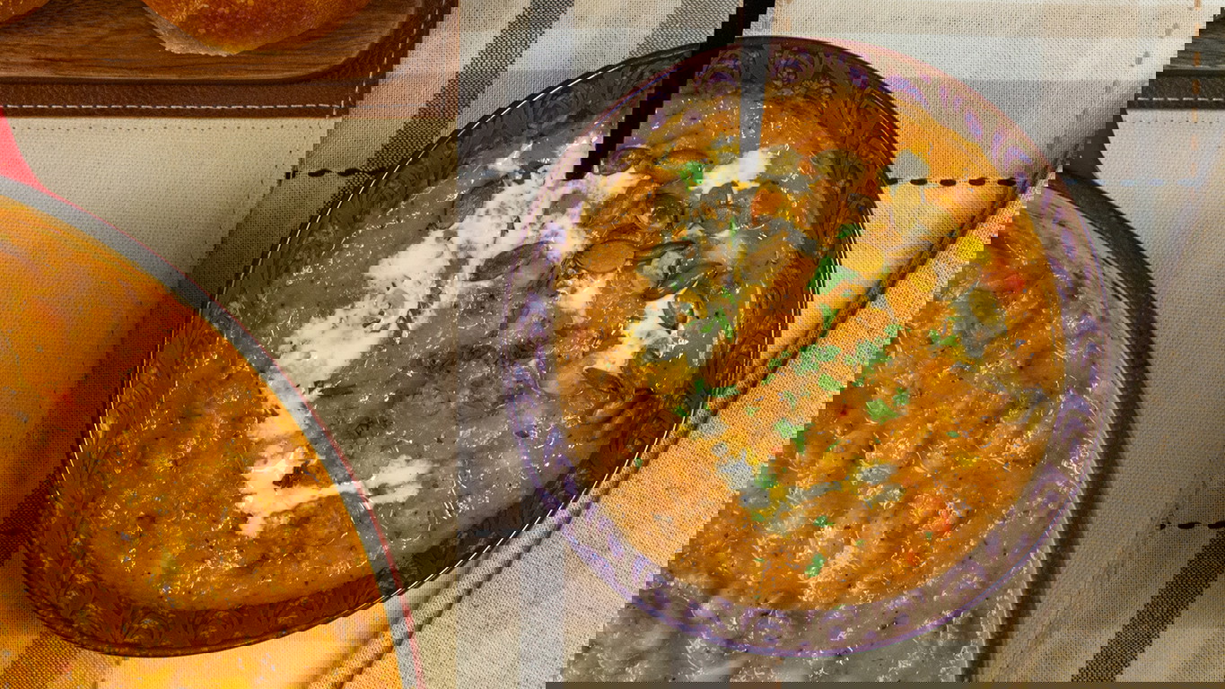 Top down image of a bowl of creamy and smooth butternut squash soup with Halal ground beef, onion, and peppers. Topped with a drizzle of cream and pumpkin seeds.