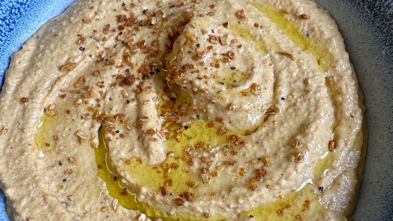 a bowl of smooth hummus drizzled with olive oil and sprinkled with hummus